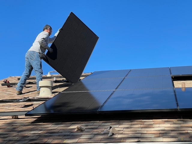 trades person stacking solar panels on roof top